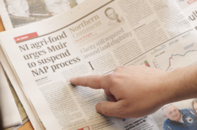 Image shows hand pointing at newspaper