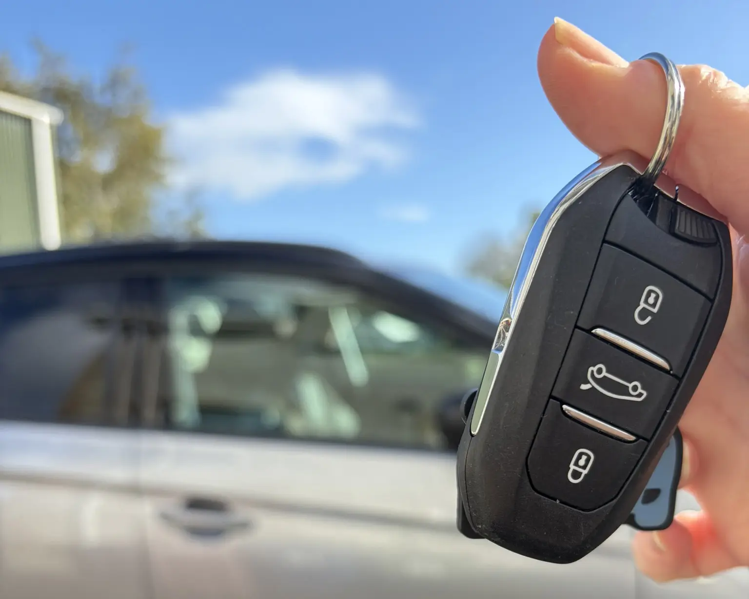Hand holding car key in front of silver car